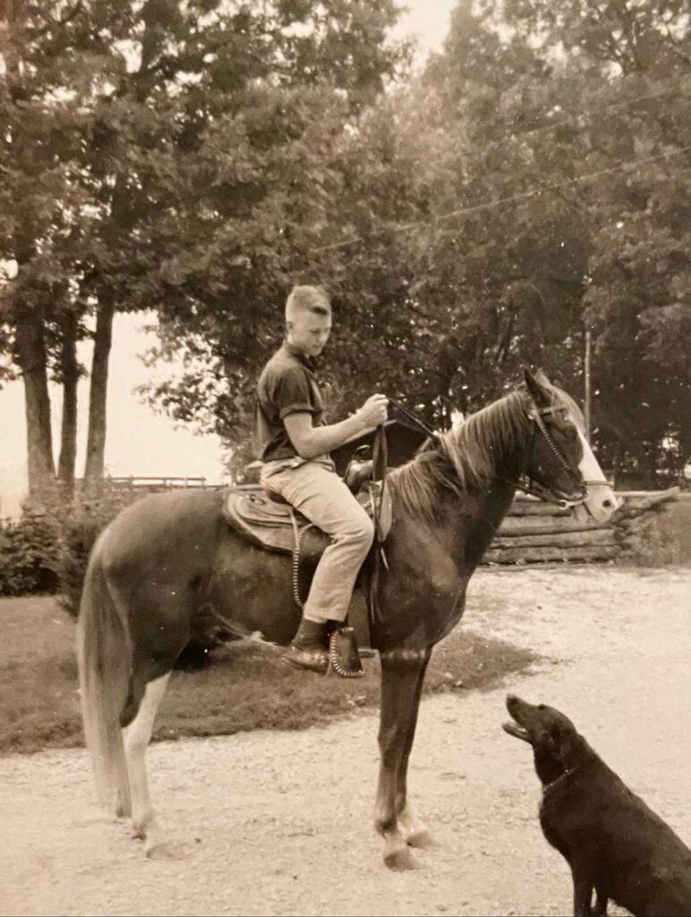 Vintage photo of young man on horse with dog looking up at him.